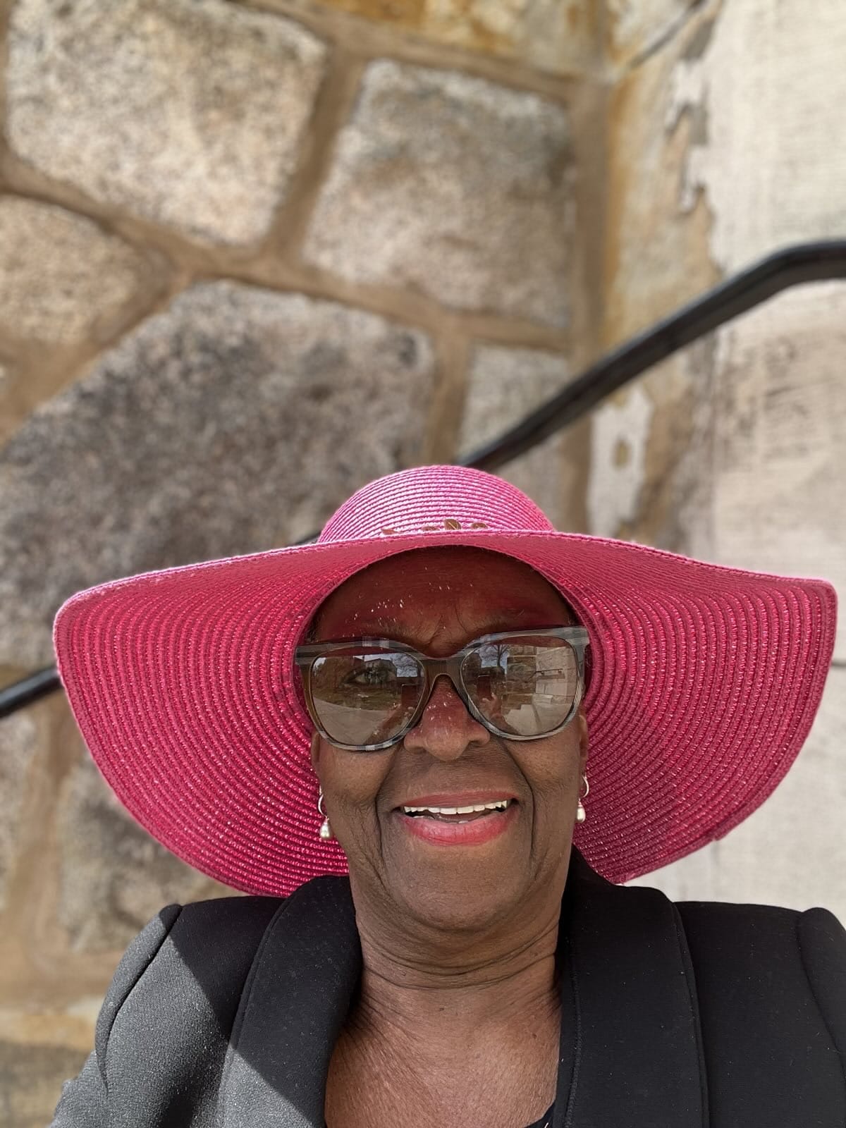 Portrait of Eva, the maker, wearing a wide-brimmed pink hat and dark sunglasses
