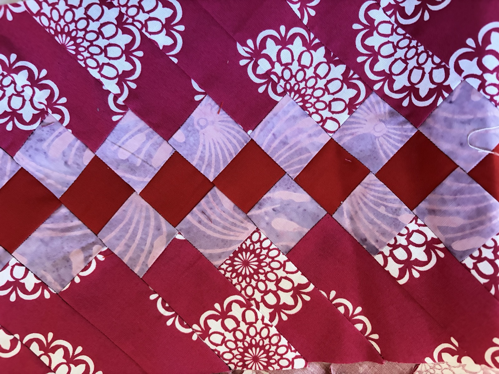 Close-up detail of a quilt in crimson, deep red, white, and lavender, with diagonal piecing and floral print