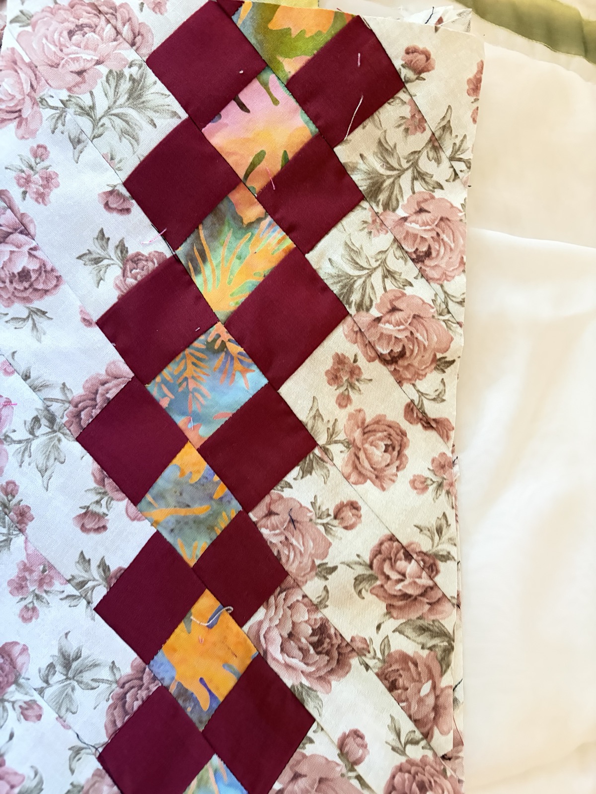 Close-up detail of a quilt with rose-print fabrics, burgundy diamond piecing, and pastel batik accents