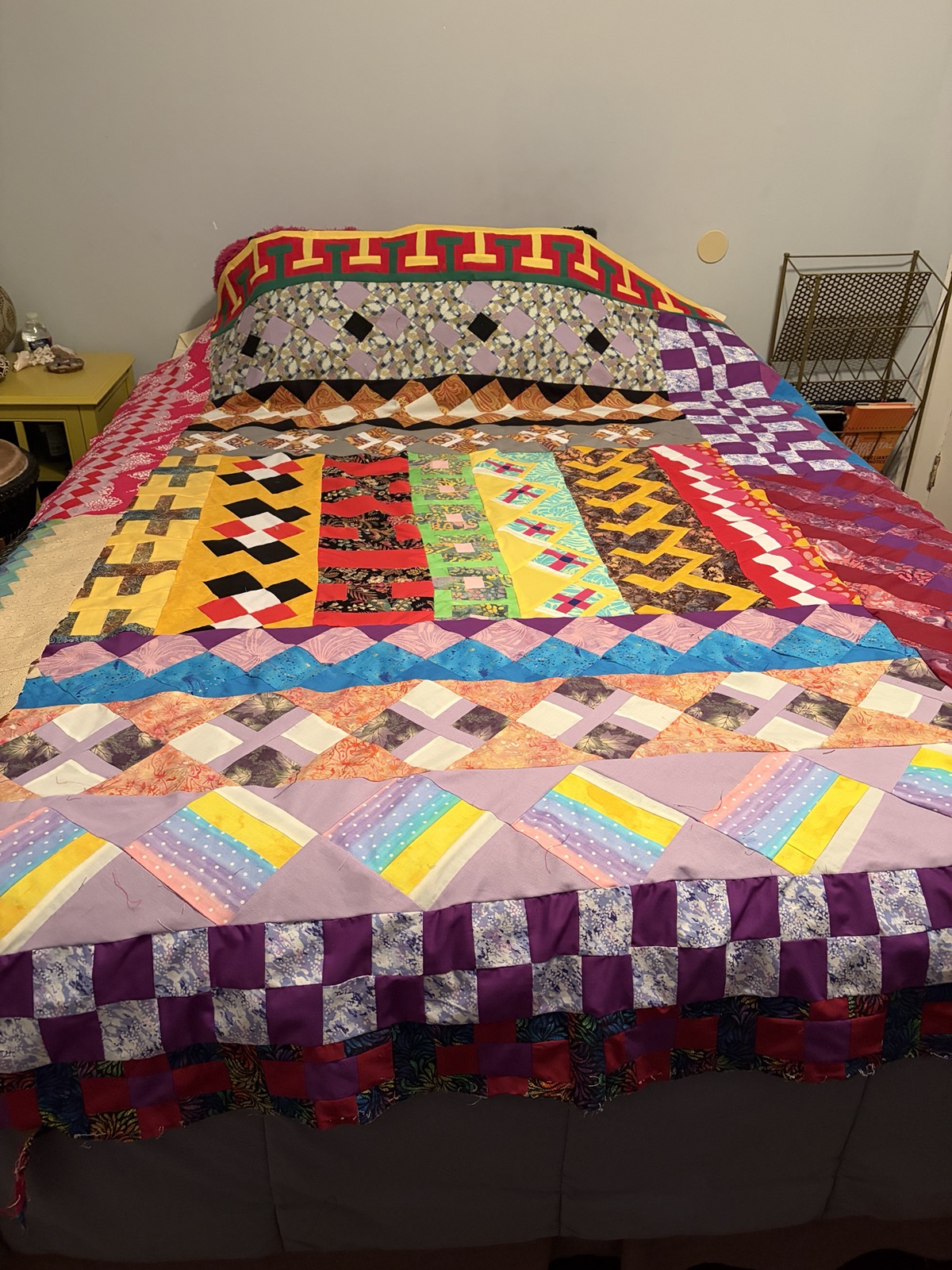 Queen-sized hand-pieced quilt with vivid patchwork blocks in purples, golds, and reds laid over a bed