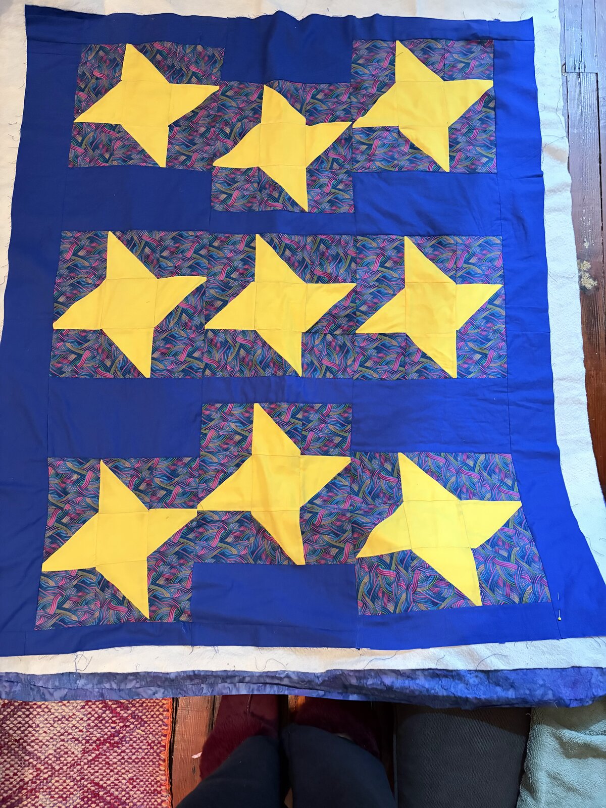Royal blue quilt top with bright yellow patchwork stars on a multicolored print background